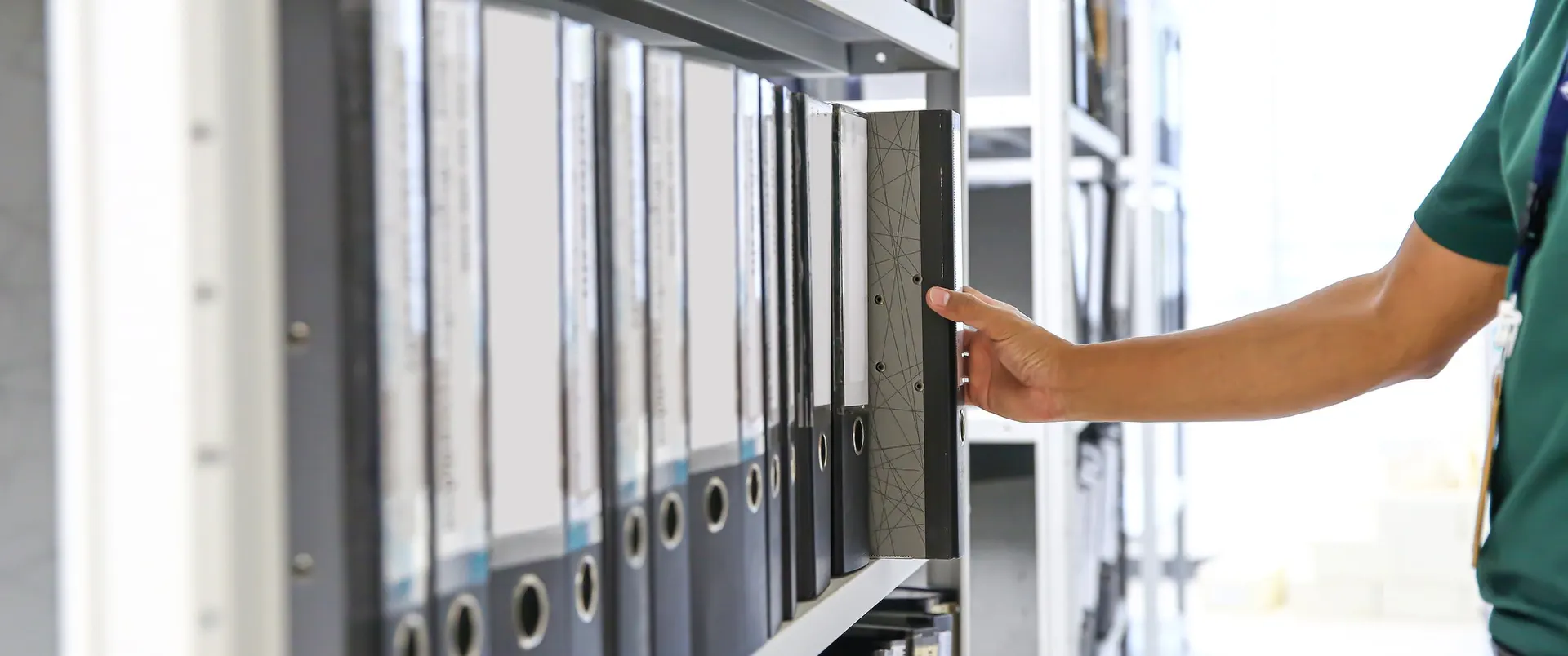 Hand selecting a folder from rows of files in a back-office archive shelf