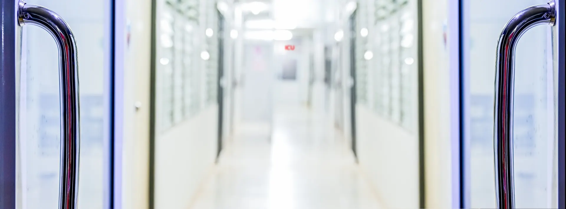 View through swing doors into a long empty hospital corridor with an illuminated ICU sign visible at the end of the hallway, evoking the operational reality behind a procurement decision